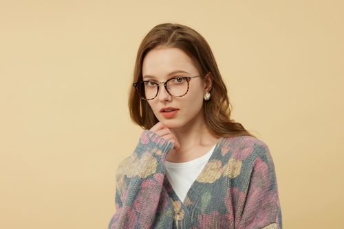 Free Elegant portrait of a young woman wearing stylish glasses and a colorful cardigan. Stock Photo