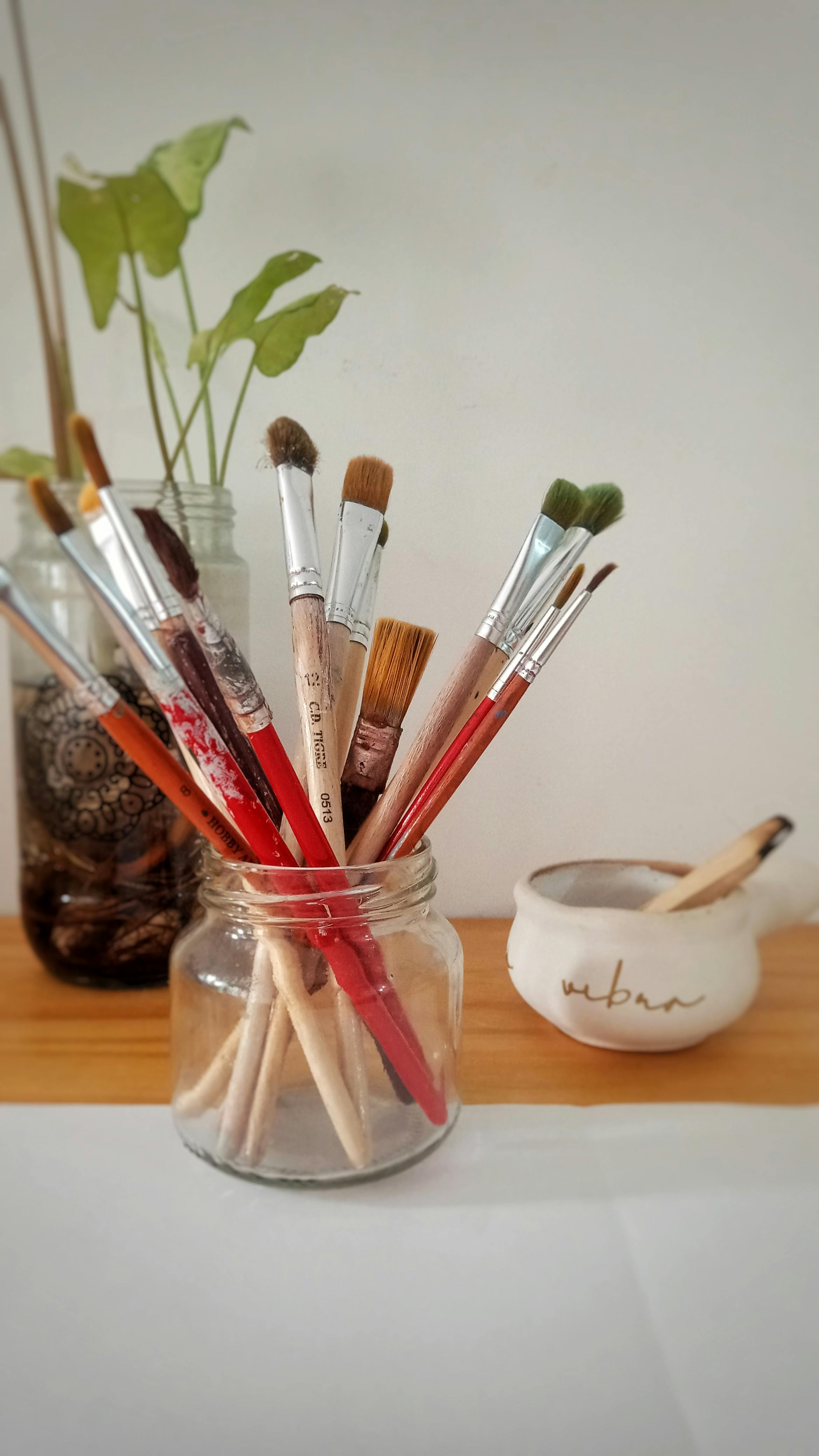 Artistic array of paintbrushes in a glass jar with plants in the background, perfect for creative inspiration.