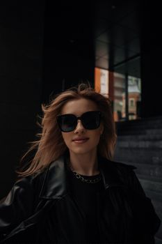 Fashionable woman with sunglasses and leather jacket in urban setting.