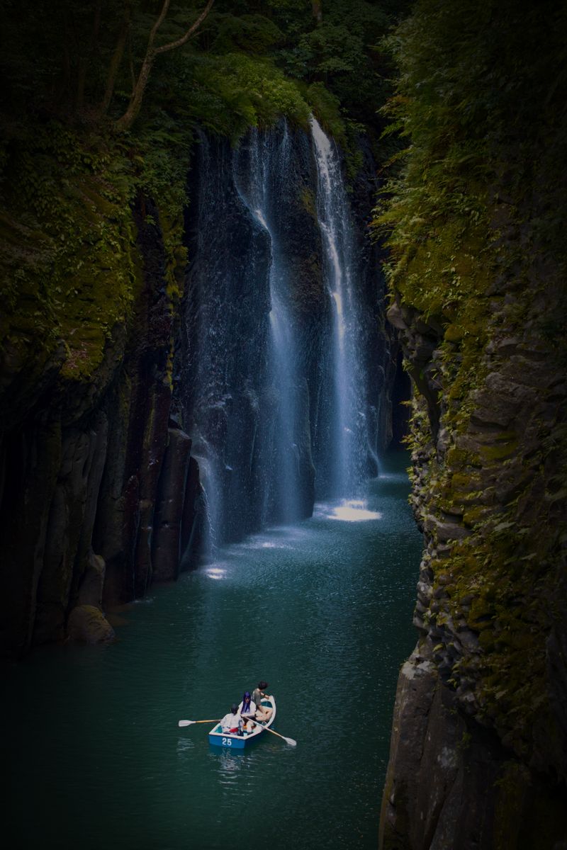 Visitors in a rental rowboat at Takachiho Gorge beneath the Manai Falls cascading between basalt columns