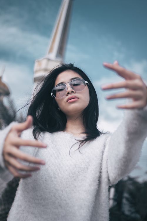 Free Young woman in sunglasses poses outdoors wearing a sweater, capturing a stylish and free-spirited vibe. Stock Photo