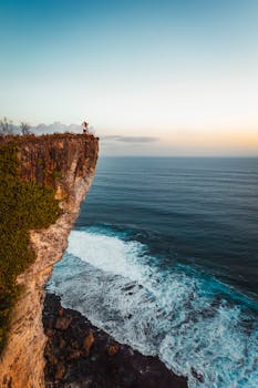 日落时分，印度尼西亚巴厘岛的一对夫妇站在引人注目的悬崖边缘，俯瞰着大海
