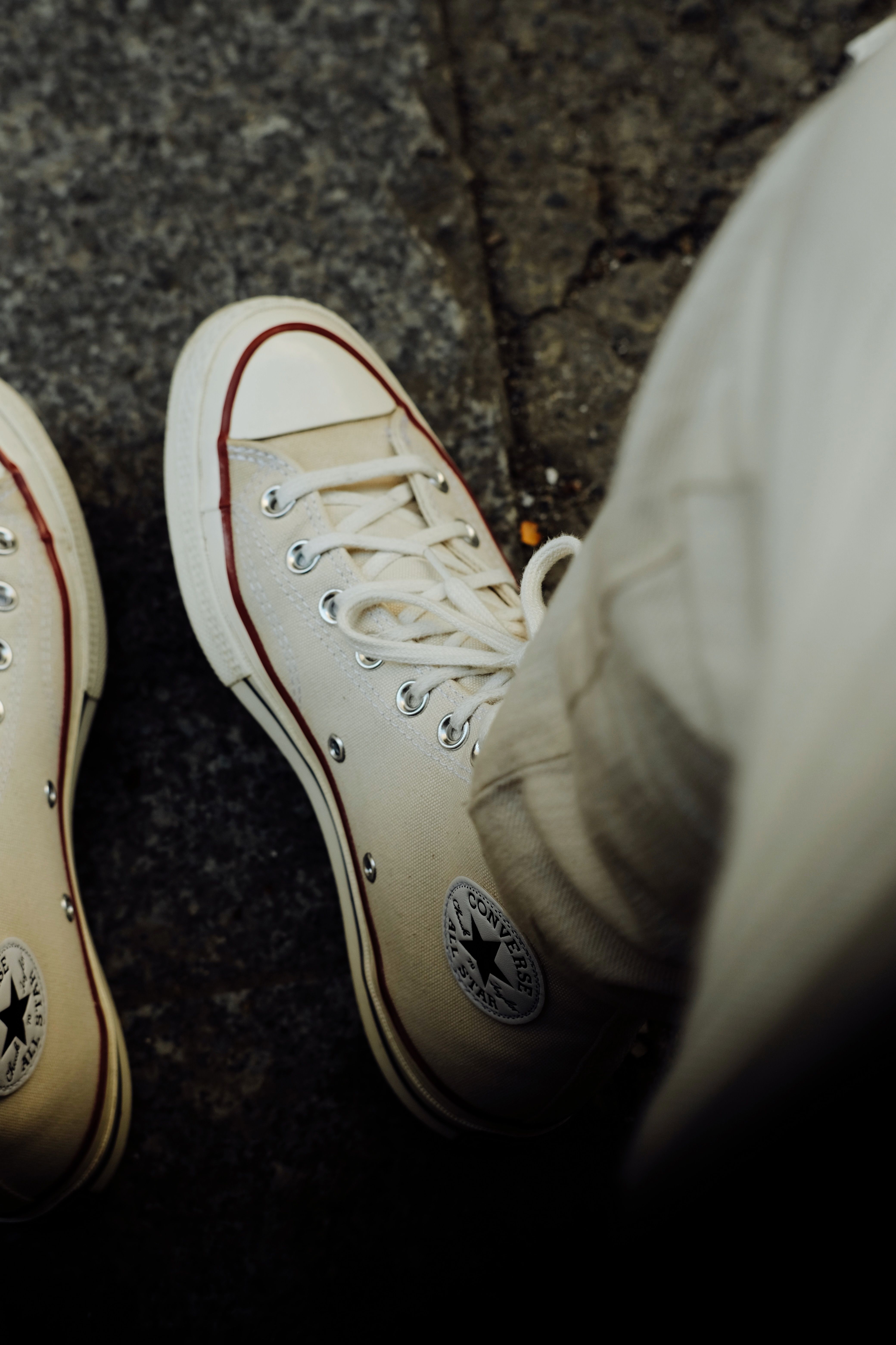 High-angle shot of classic white canvas sneakers on a pavement, showcasing casual street style.