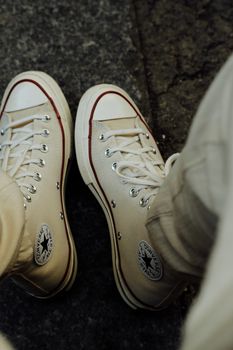 Top view of person wearing stylish white sneakers on a textured floor.