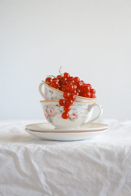Red currants elegantly piled in decorative vintage tea cups on a tablecloth.
