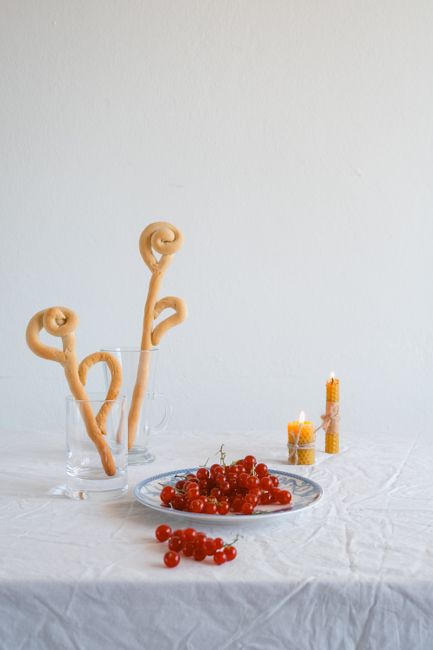 Elegant still life featuring dough shapes in glasses, red currants on a plate, and lit candles for a cozy ambiance.