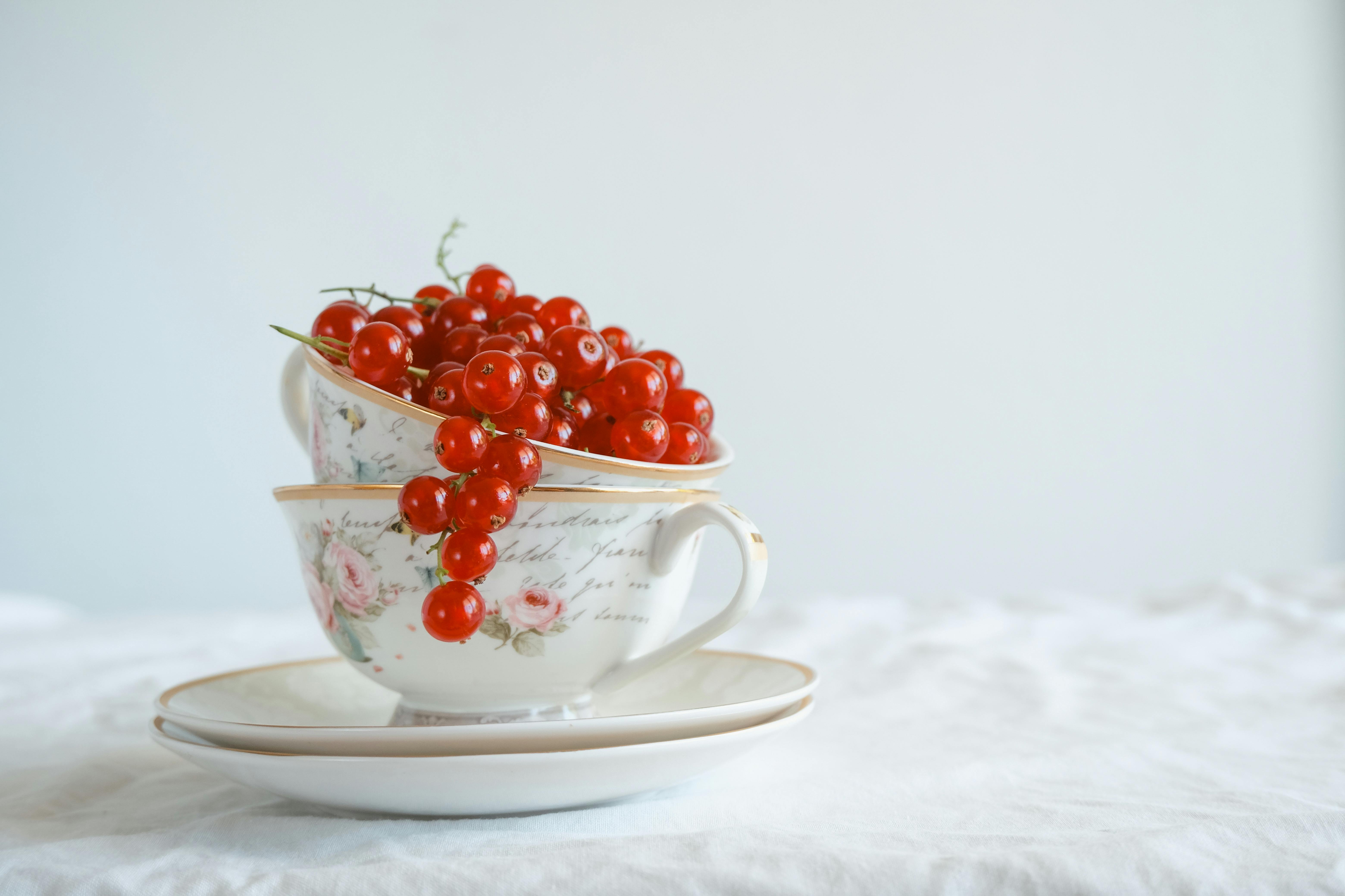 Aesthetic display of red currants in vintage cups on a white tablecloth, perfect for food photography.