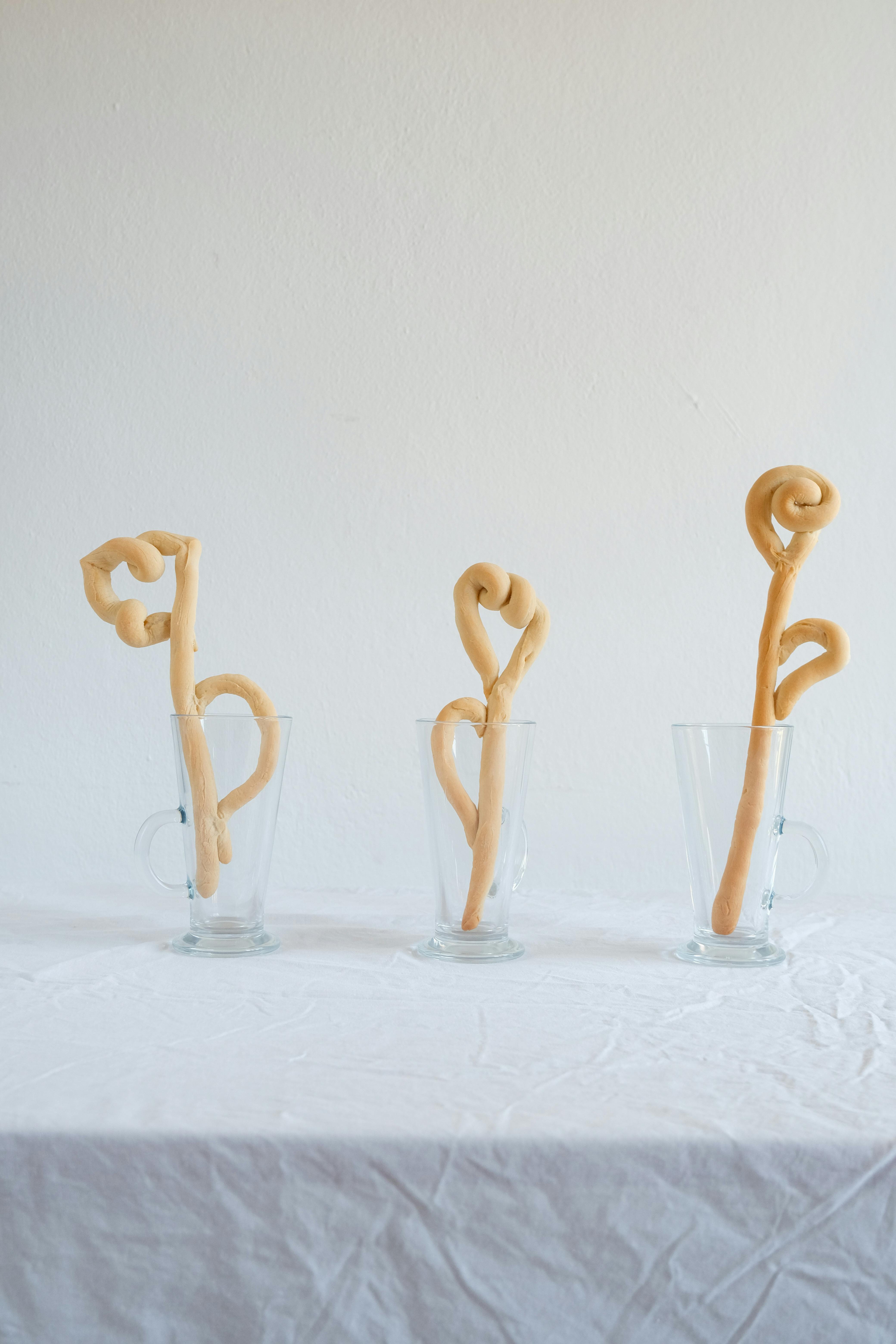 Sculpted dough art in three clear glass mugs, displayed on a white table.