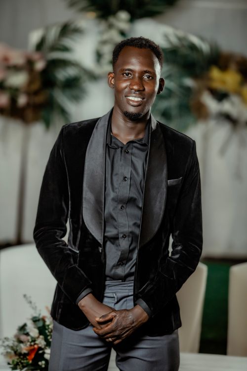 Free A stylish portrait of a man in a black velvet suit, standing indoors with a floral backdrop. Stock Photo
