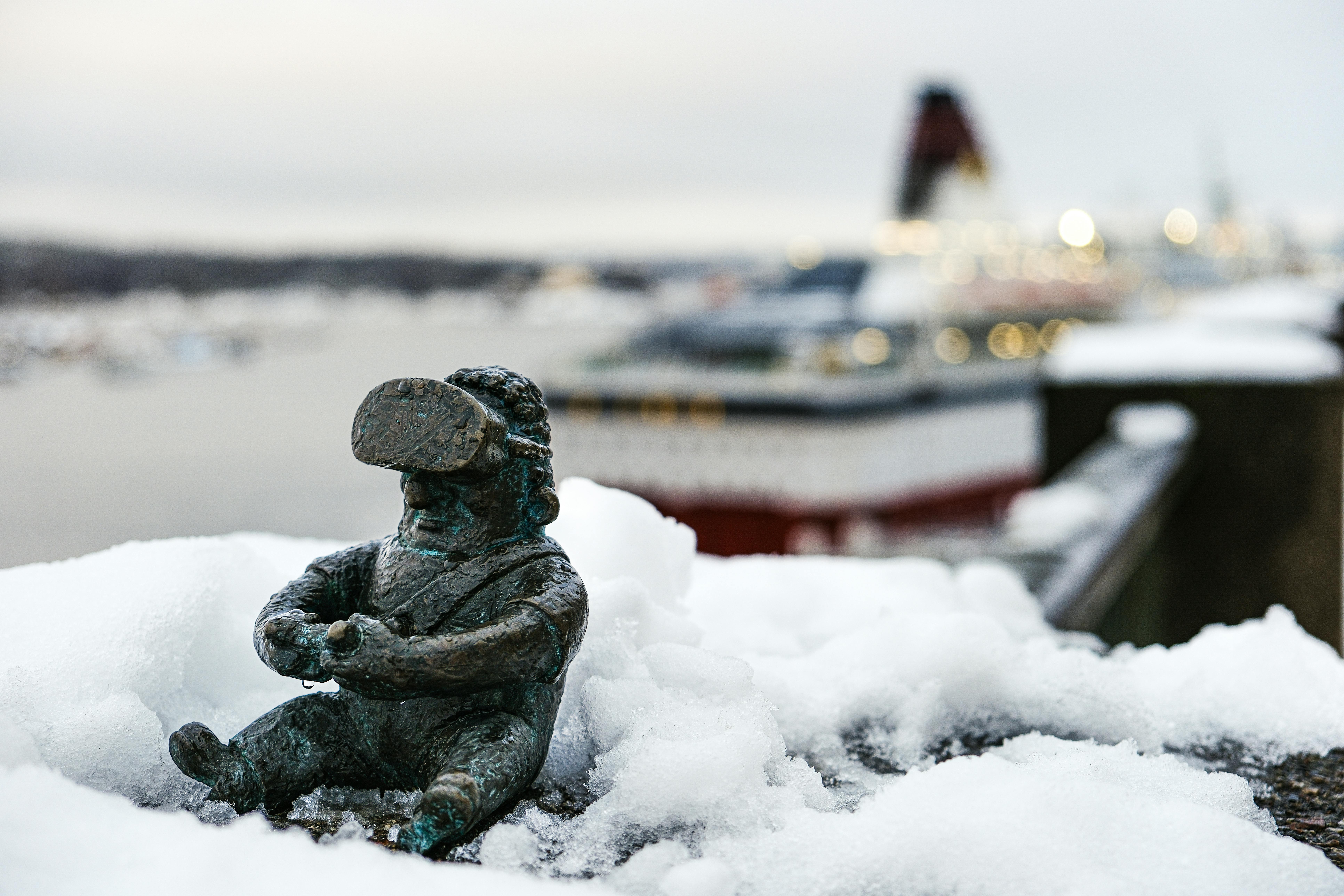 Free A small snow-covered statue near a large ship in a winter setting, perfect for travel and winter themes. Stock Photo