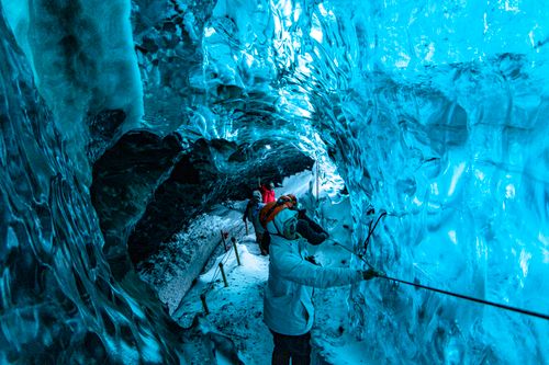 Free Group exploring a stunning blue ice cave, showcasing glacial textures and colors. Stock Photo