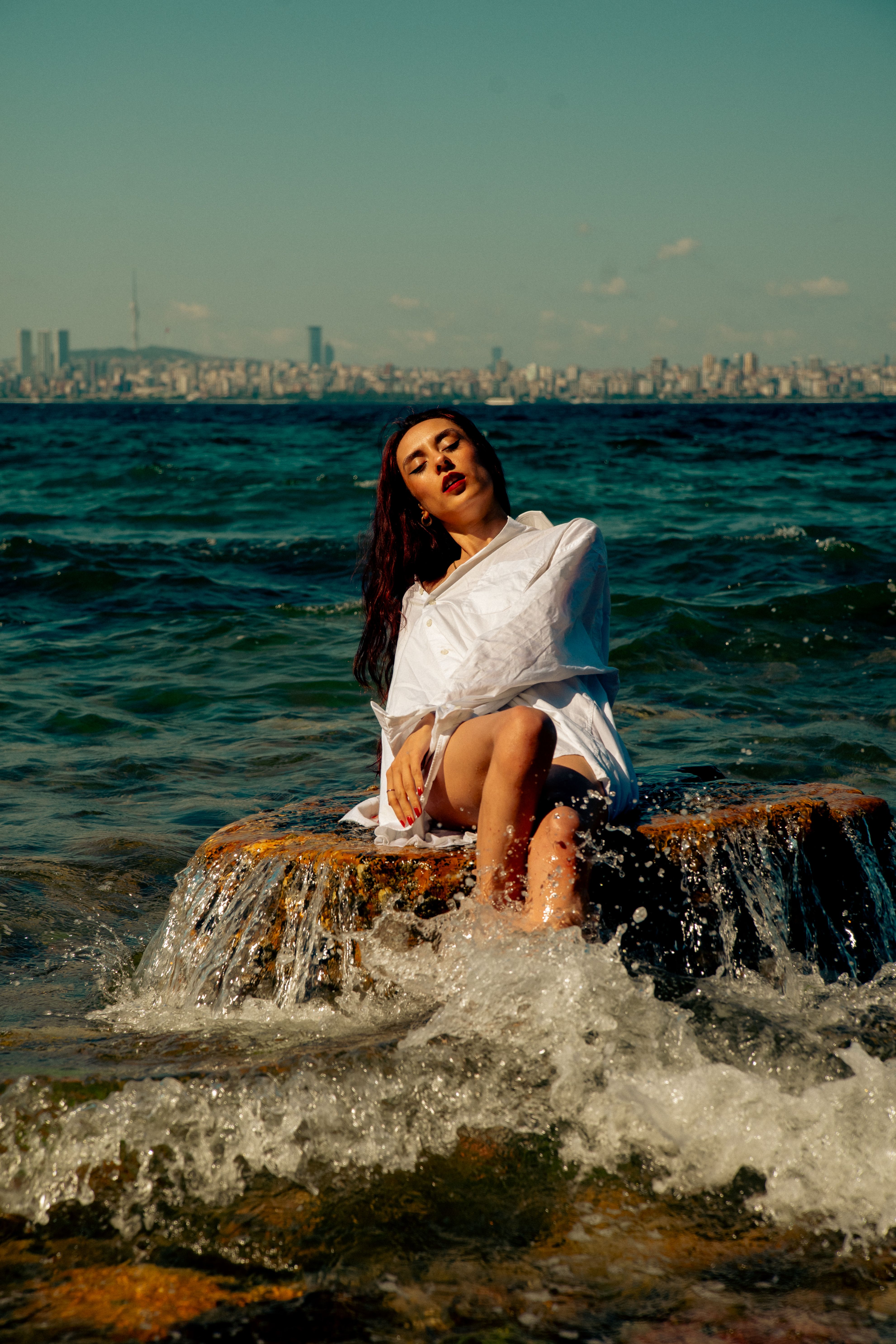 Brunette woman in a white shirt posing on a rock by the seaside, summer vibes.