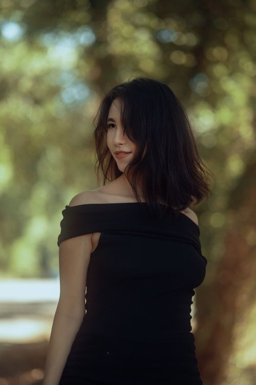 Free A brunette woman in a black dress posing gracefully in an outdoor park setting. Stock Photo