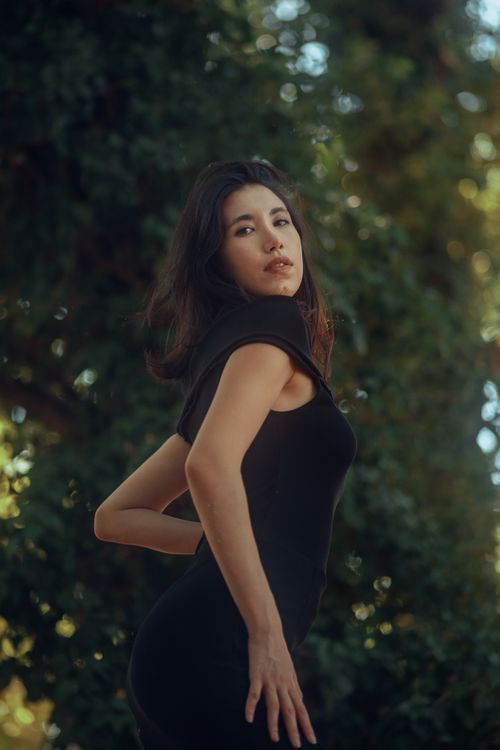 Free Portrait of a woman posing gracefully outdoors with lush greenery. Stock Photo