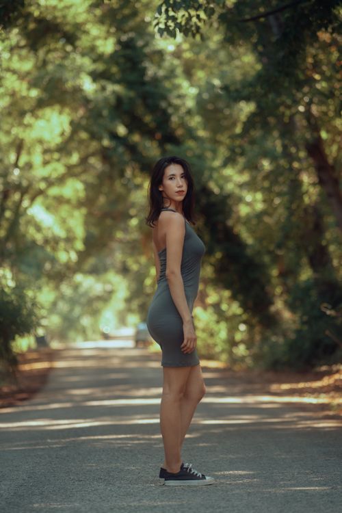 Free A young woman posing confidently on a sunlit forest road during summer. Stock Photo