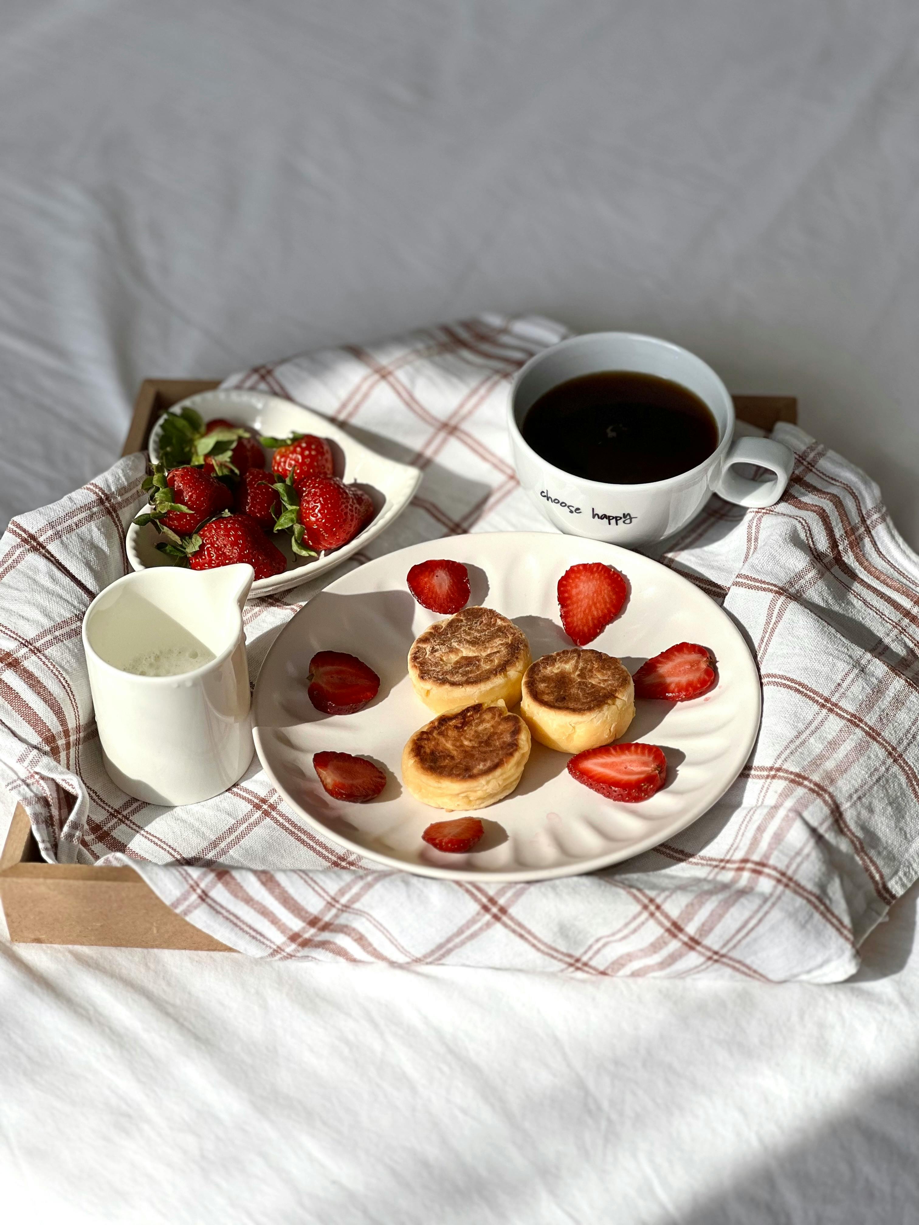 A breakfast setup with English muffins, strawberries, coffee, and milk on a tray.