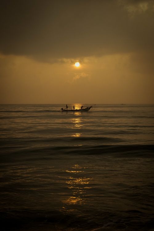 Free Silhouetted fishermen on a boat during sunrise over the calm seas of Chennai, India. Stock Photo