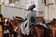 Colorful traditional horseback parade in urban street with riders in vibrant attire.