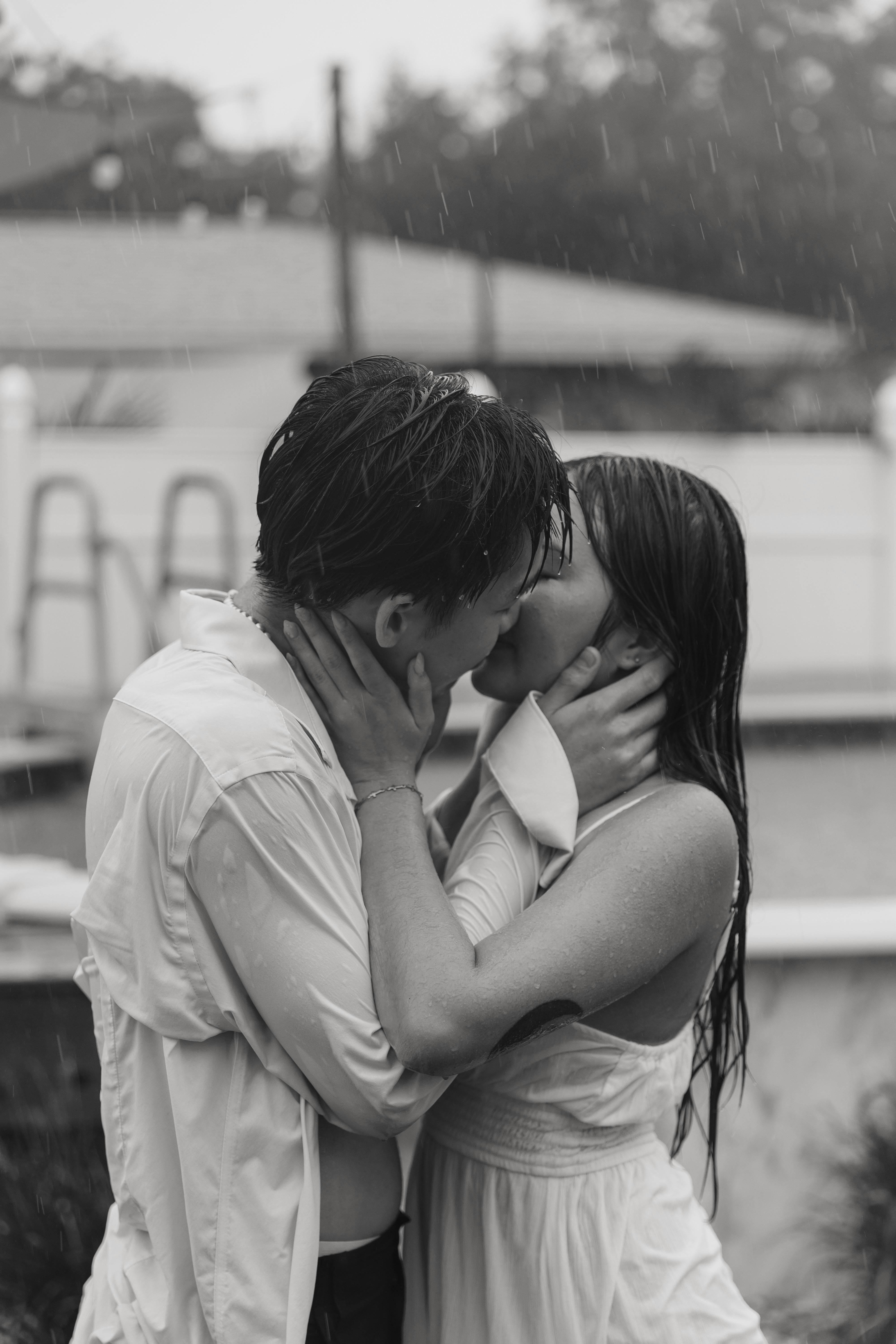 A couple sharing a passionate kiss outdoors in the rain, captured in black and white.