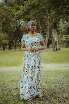 A woman in a floral dress stands gracefully in a lush, green outdoor setting.