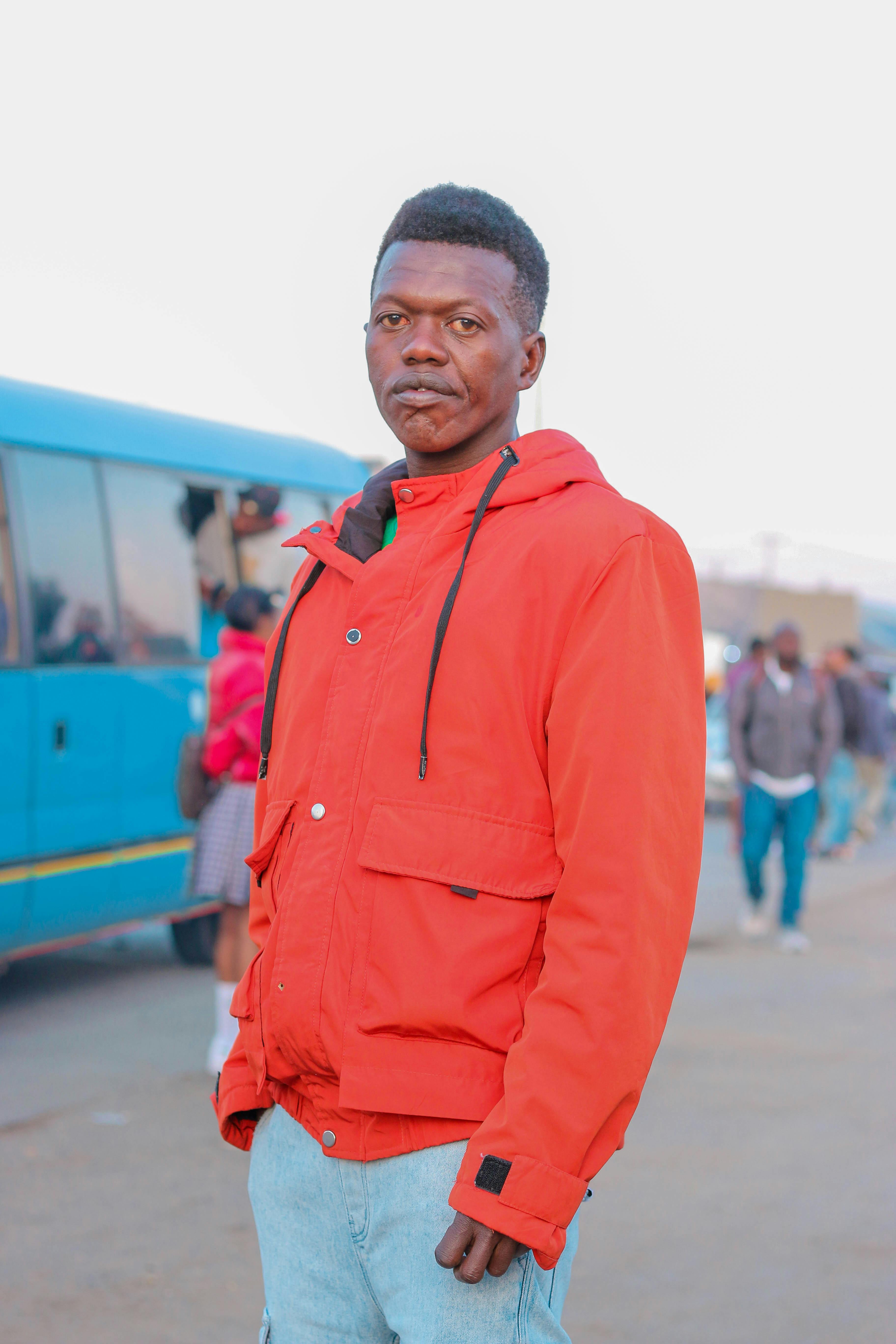 A man in an orange jacket stands outdoors beside a blue van, capturing a vibrant street scene.