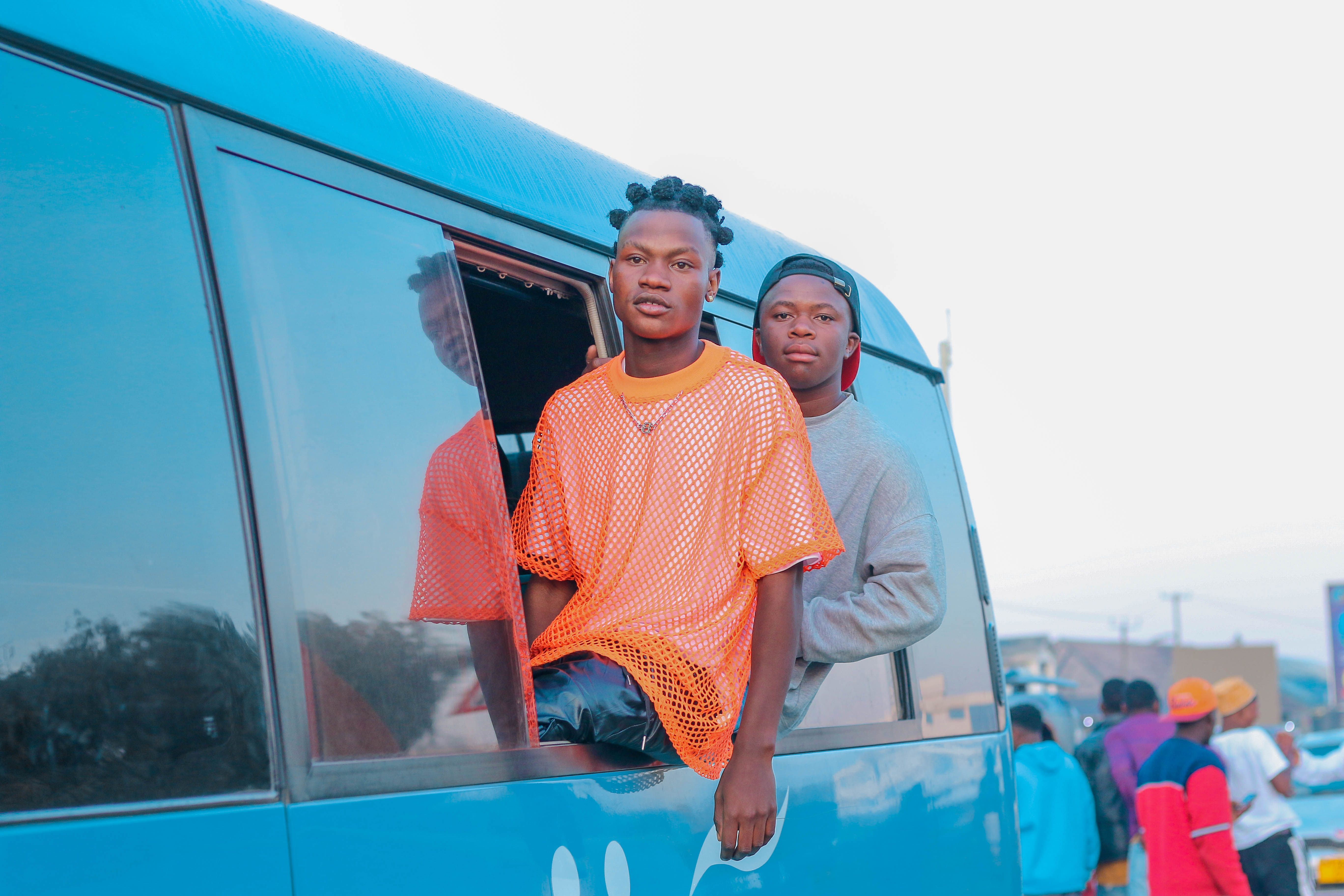 Two young men looking out the window of a blue van on a sunny day.