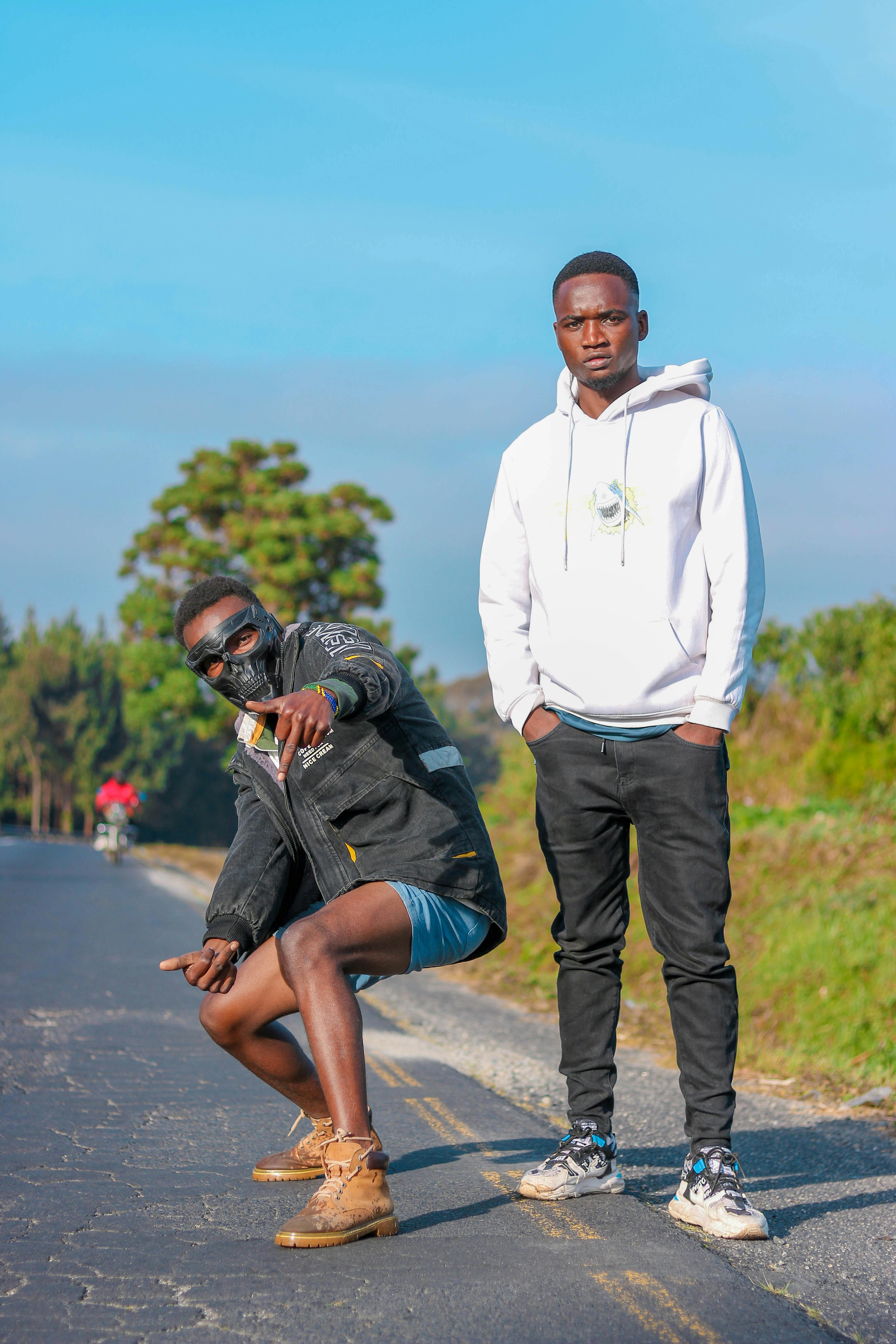 Two young African men in casual outfits posing confidently on a sunny day outdoors.