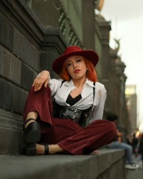 Stylish redhead woman in urban setting with confident pose wearing a fashionable hat.