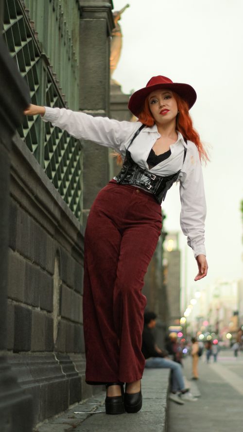 Free Stylish urban fashion photo of a red-haired woman in red hat and pants leaning on a city building. Stock Photo