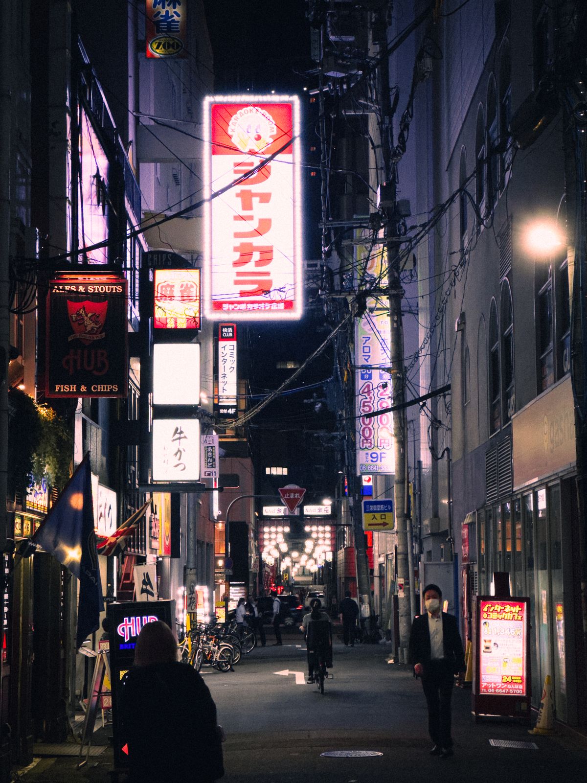 A lively illuminated alley in Osaka at night with glowing neon signs and people passing by