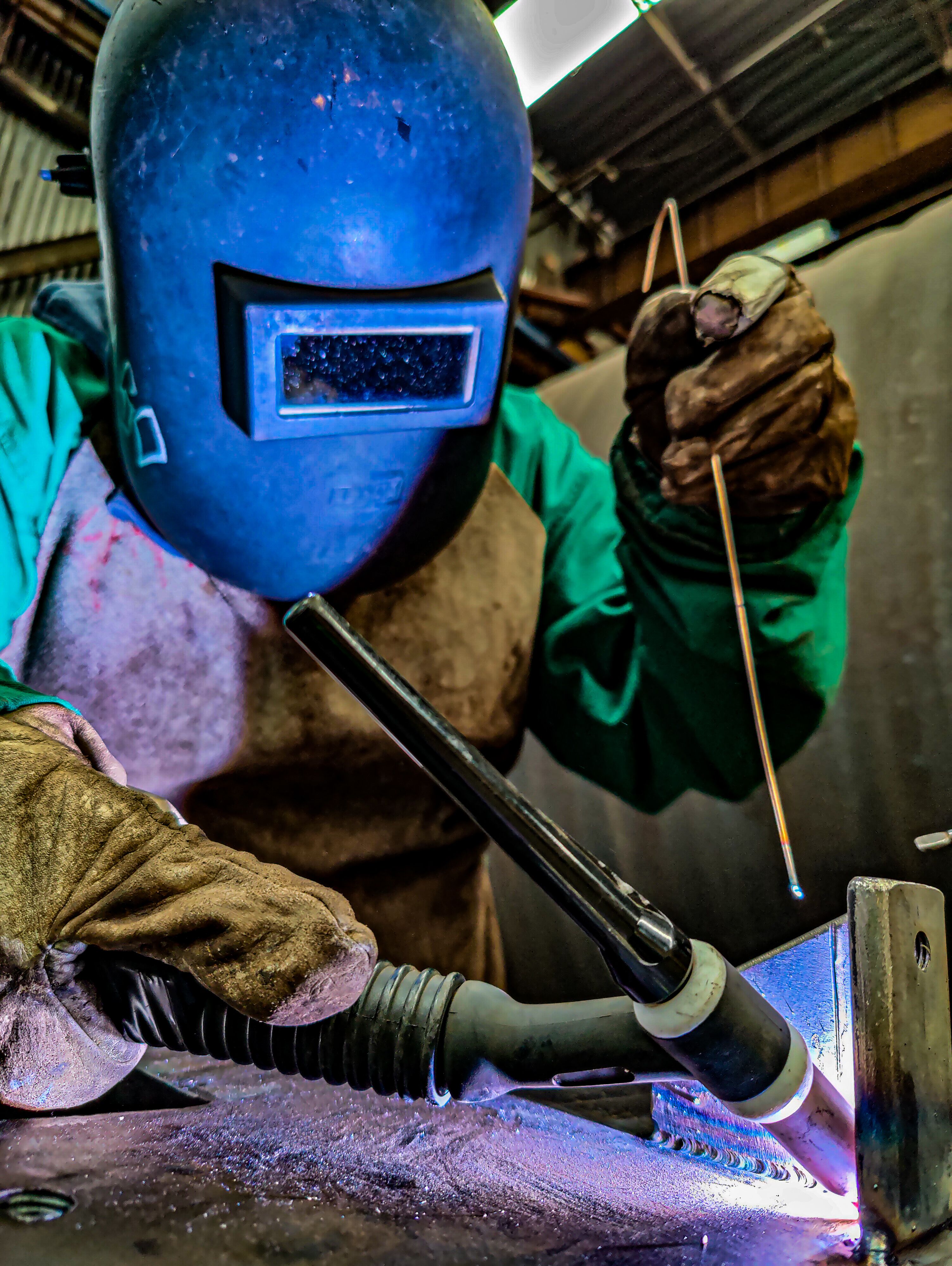 Sudor cu echipament de protecție lucrând concentrat la o îmbinare metalică, cu scântei aprinse în jur