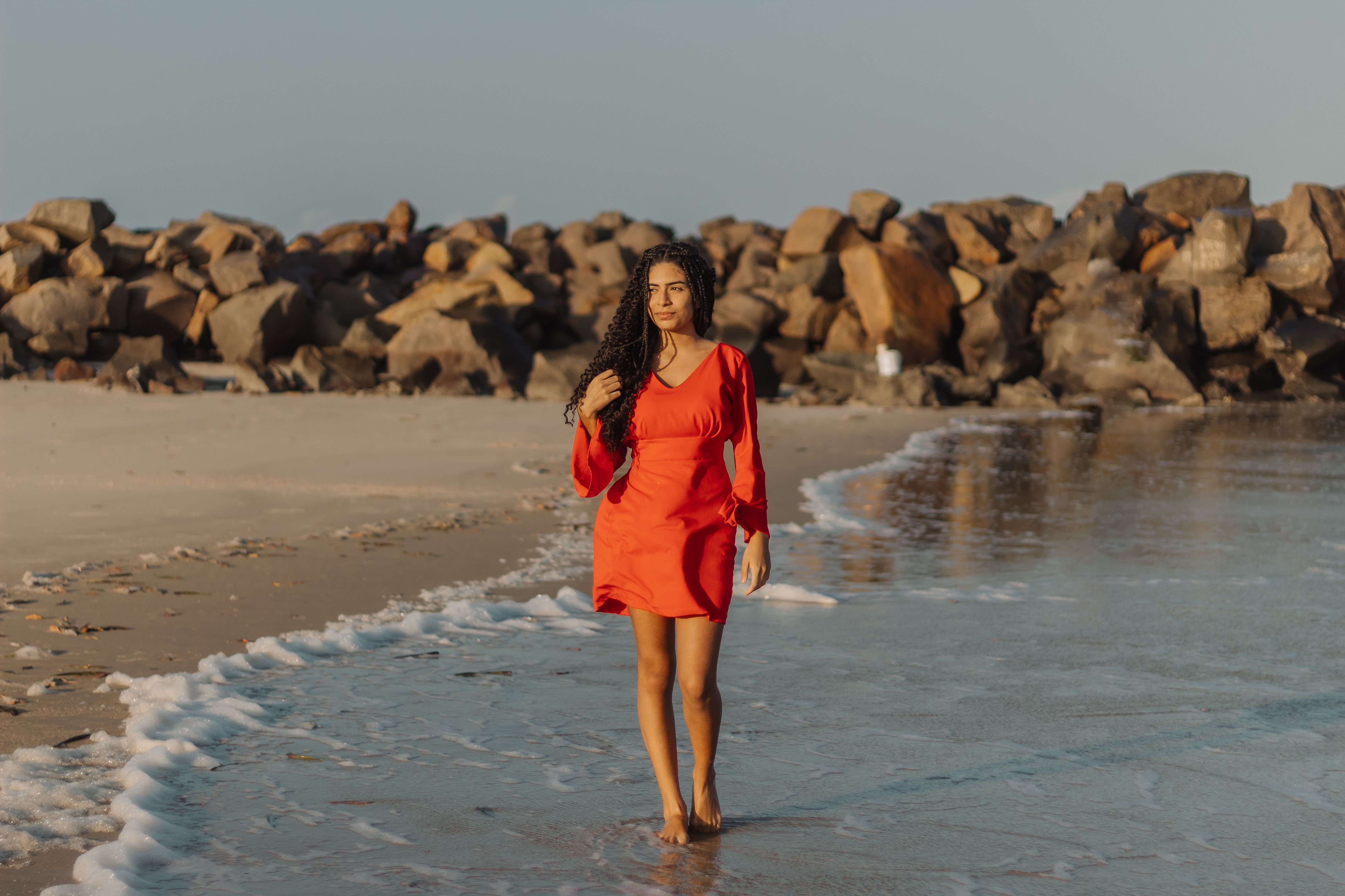 A woman in an orange dress walking on the beach · Free Stock Photo