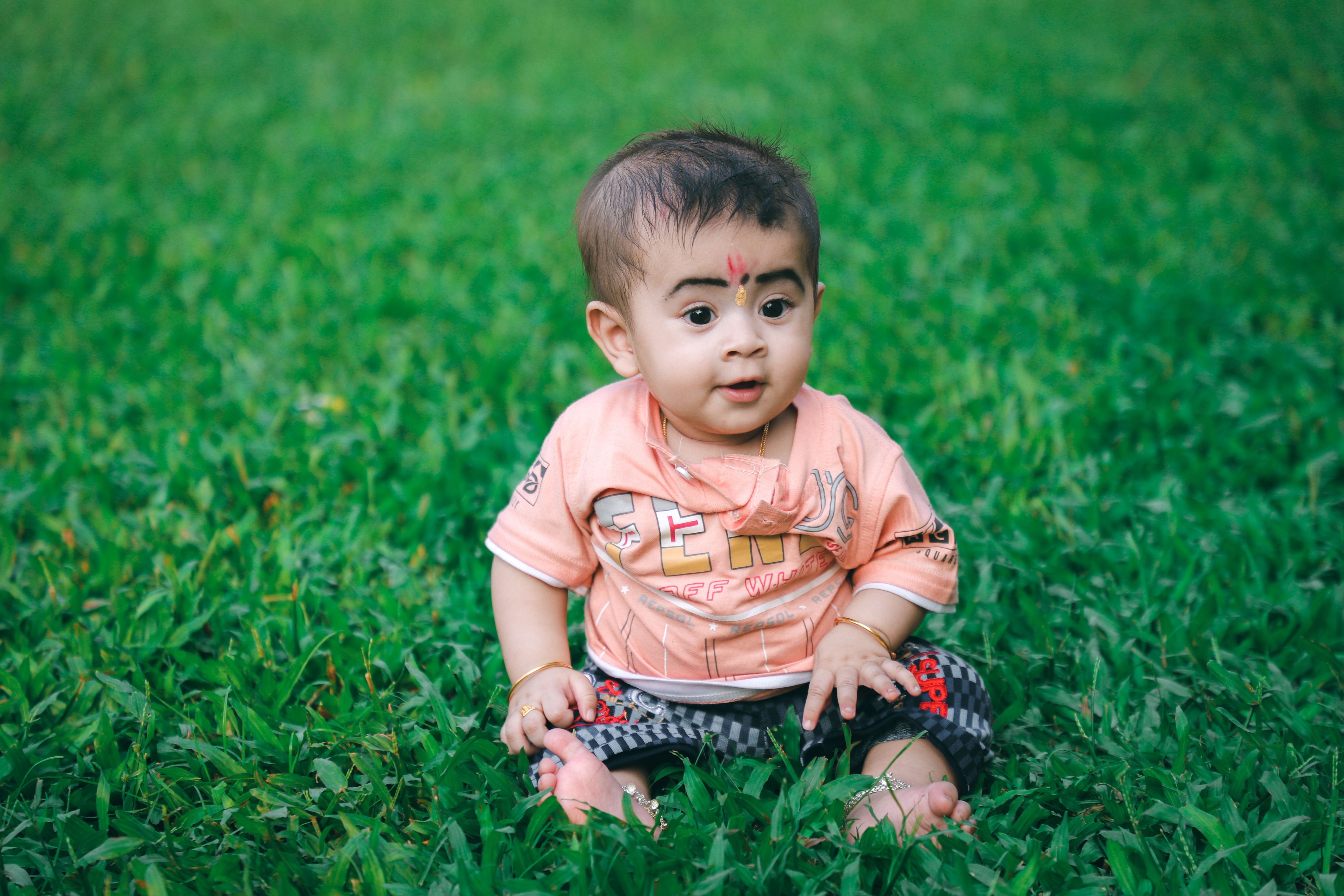 A baby sitting on the grass in front of a tree