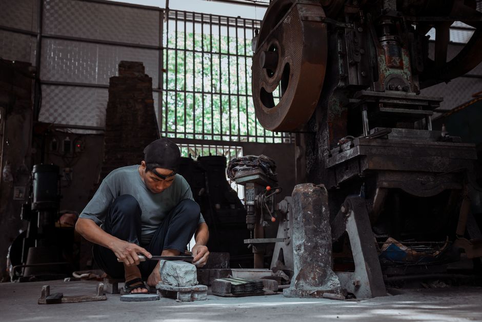 Dedicated artisan concentrating on metalwork tasks inside a workshop filled with machinery.