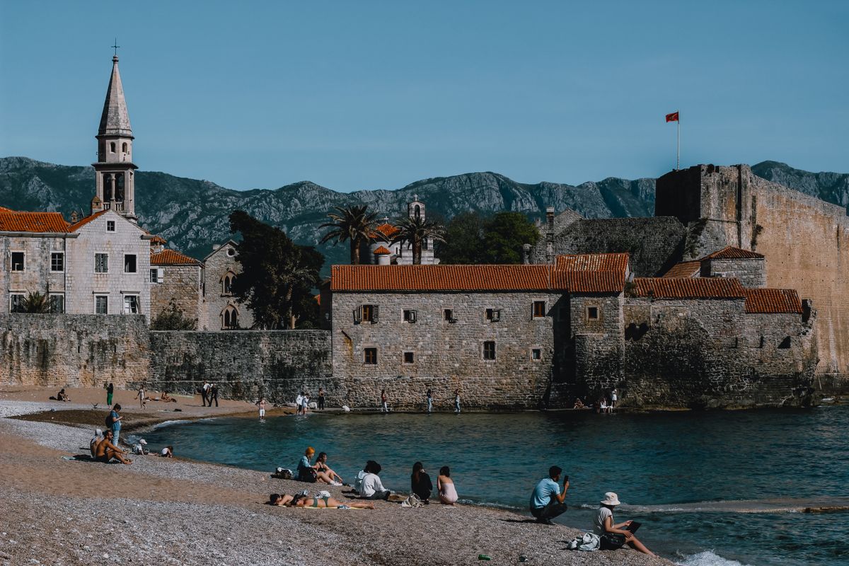 A beach with sunbeds directly below the walls of Budva old town
