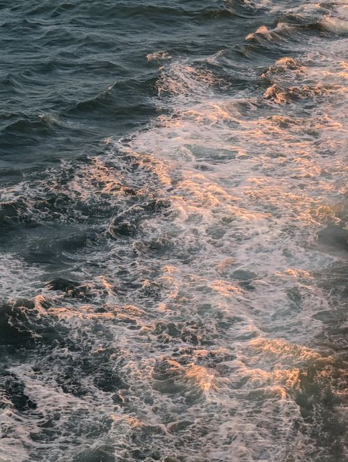 Free Close-up of ocean waves glistening in the sunset light, showcasing vibrant, golden hues and foamy textures. Stock Photo