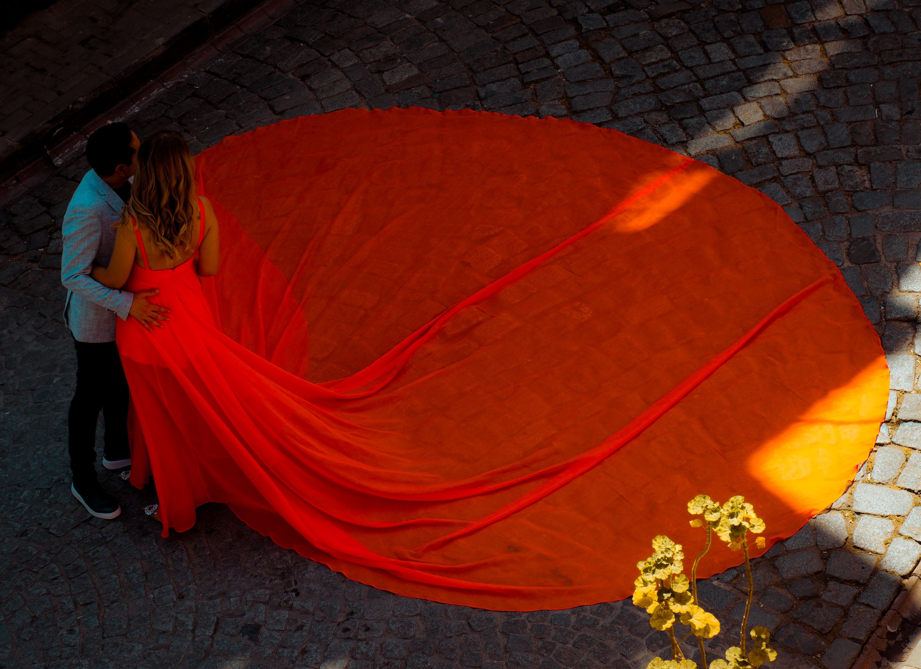 Elegant couple posing on cobblestone in a vibrant red gown capturing a romantic moment.