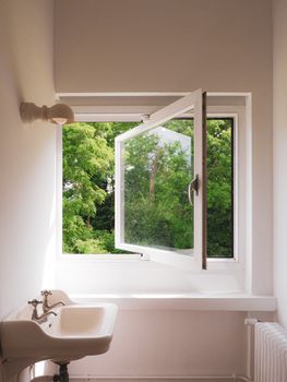 Simple white bathroom with a view of greenery through an open window.
