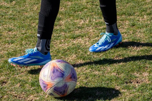 Close-up of a soccer player's feet in blue cleats on a grassy field with a colorful soccer ball.