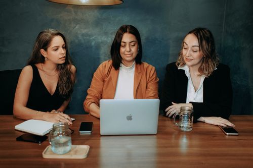 Free Three women engaged in a focused business meeting at a modern office setting with laptops and notebooks. Stock Photo