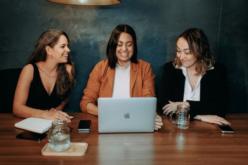 Free Three women enjoying a collaborative meeting in a modern office setting, using laptops and smiling. Stock Photo