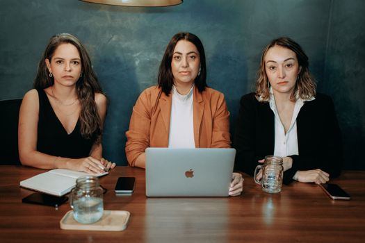 Three serious women in formal wear at a business meeting with laptops and notebooks.