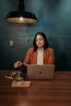 A woman working on a laptop at a wooden desk under a stylish lamp, in a modern office setting.