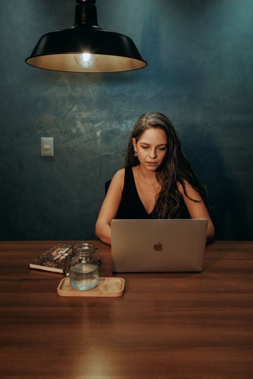 Free Young woman working intently on a laptop under warm lighting in a modern interior setting. Stock Photo