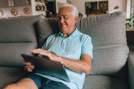 Senior man relaxing on a sofa using a tablet, enjoying technology at home.
