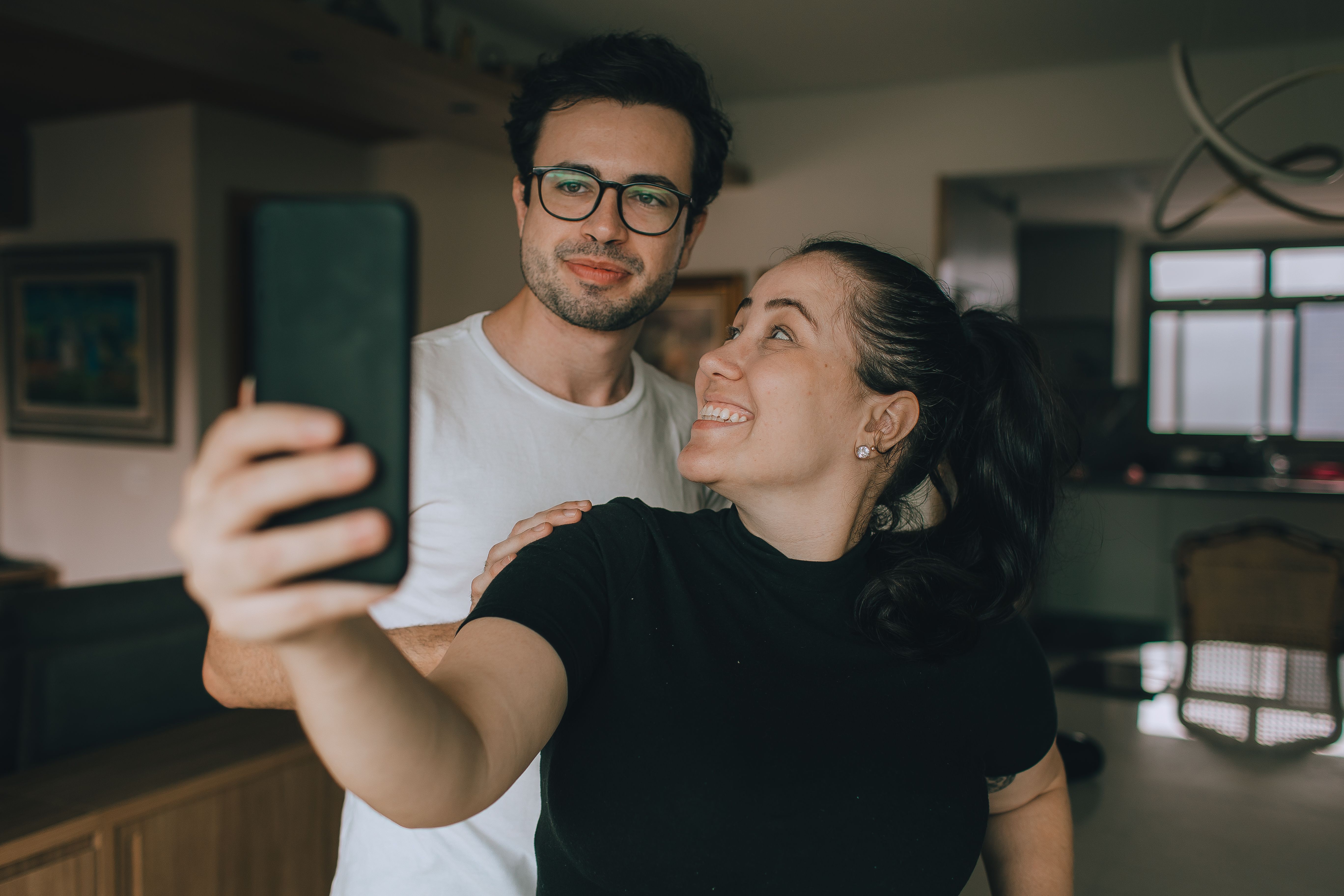 A cheerful couple takes a selfie in their cozy living room, enjoying a moment together.