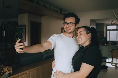 Free Smiling couple embraces while taking a selfie in their cozy modern home interior. Stock Photo