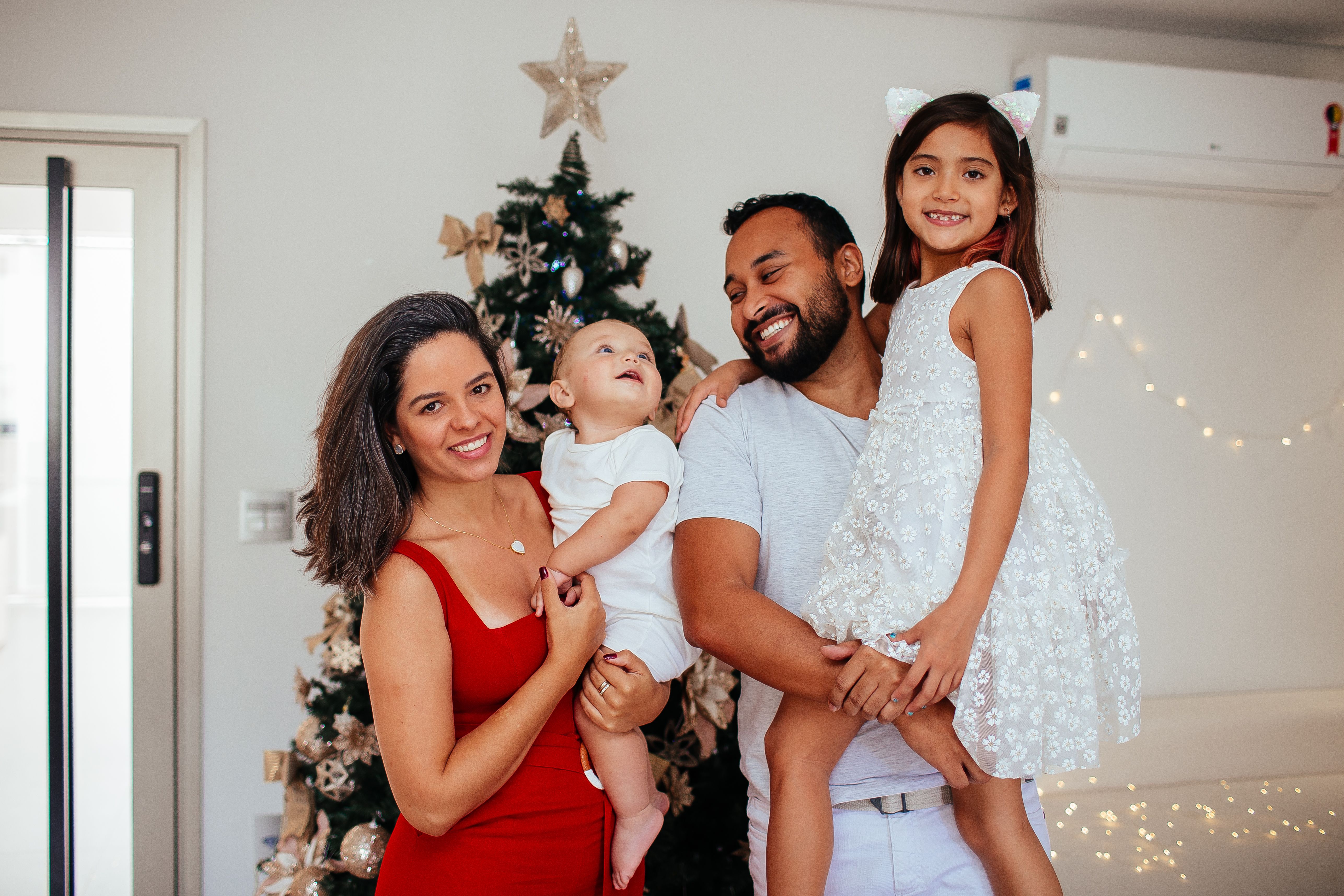 happy family with a baby standing together in front of a decorated Christmas tree during a calm holiday gathering