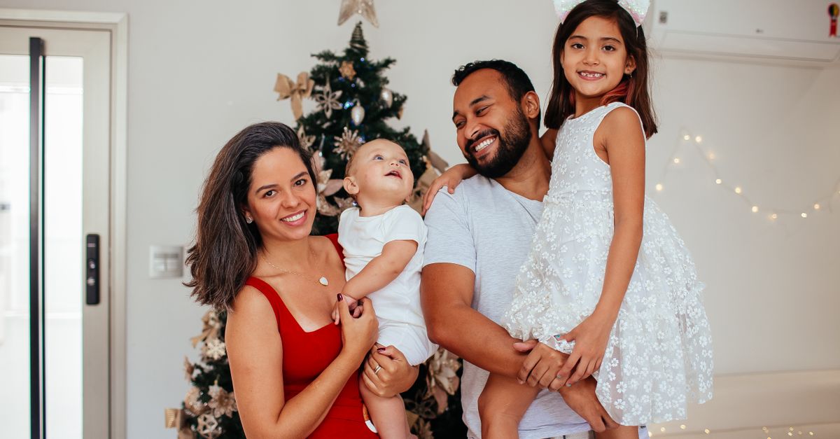 happy family with a baby standing together in front of a decorated Christmas tree during a calm holiday gathering