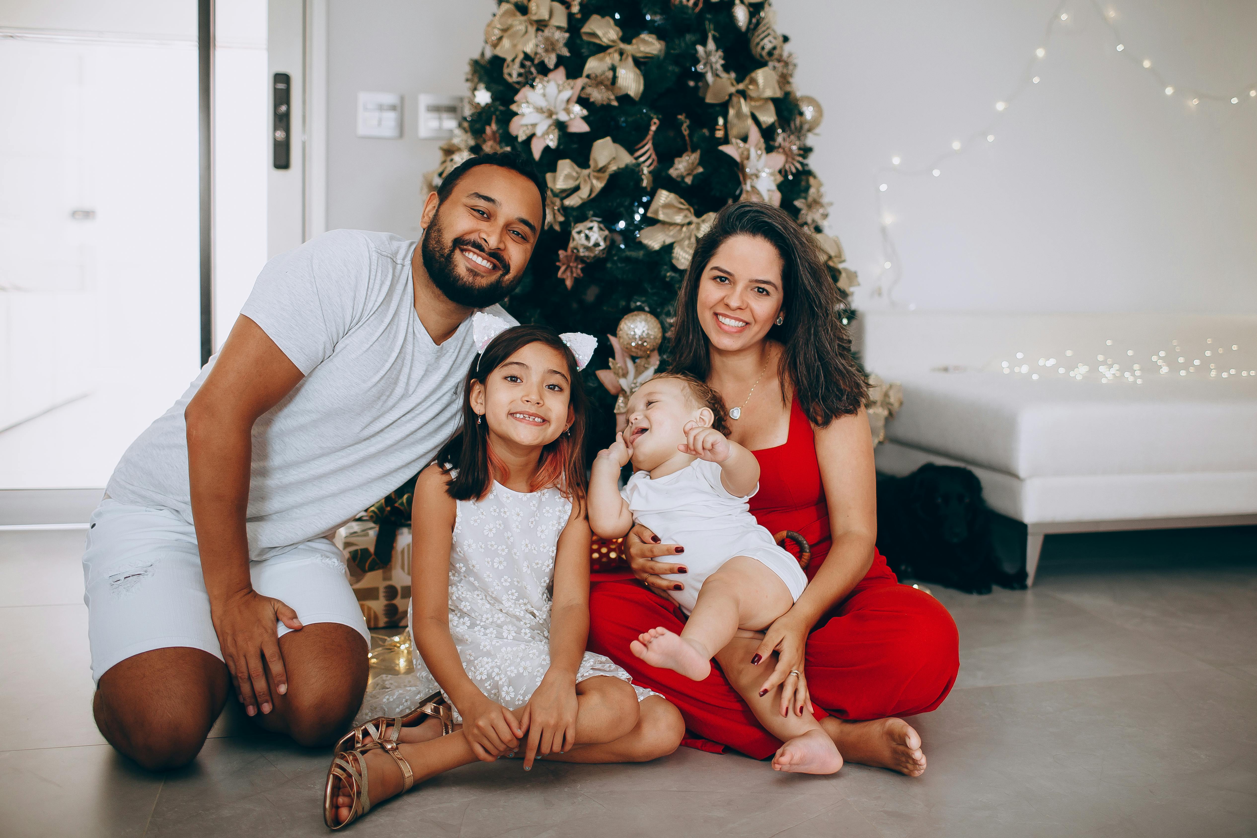 Family gathered around Christmas tree with decorations, sharing joy and smiles indoors.